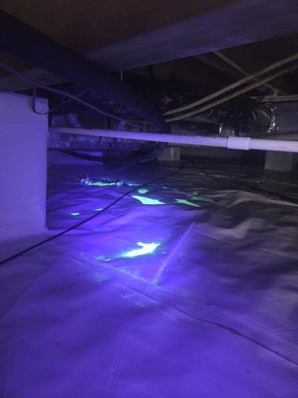 Responded to report of yellow-green fluid leak in crawl space. Upon inspection, utilized UV lighting to identify and locate condensate drainage issue. Fluorescent tracer dye revealed active condensate leak from HVAC system draining onto vapor barrier in crawl space. Documented leak location and extent of moisture intrusion with photographic evidence showing multiple concentration points of fluorescent material on floor covering beneath air handler and condensate drain line.