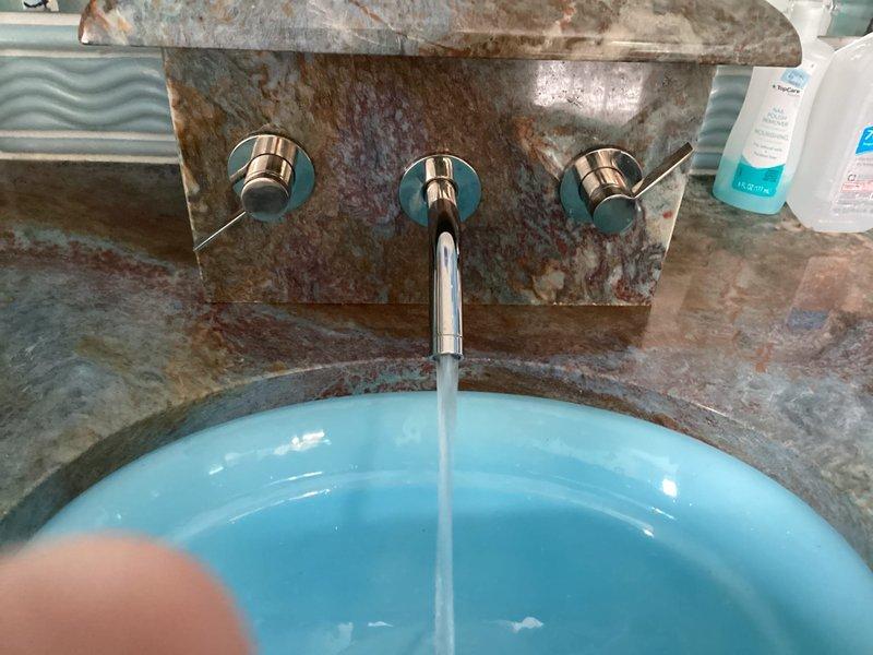 Responded to service call for difficult-to-operate cold water faucet handle in master bathroom. Upon inspection, found wall-mounted three-piece faucet assembly with separate hot and cold control valves and center spout. Diagnosed stiff cold water valve operation likely caused by mineral buildup or worn internal cartridge components. Disassembled cold water control valve, inspected cartridge mechanism, cleaned mineral deposits, and lubricated moving parts. Tested valve operation to ensure smooth handle rotation and proper water flow control. Verified no leaks at valve body or wall connections. Faucet now operates smoothly with full range of motion restored to cold water handle.