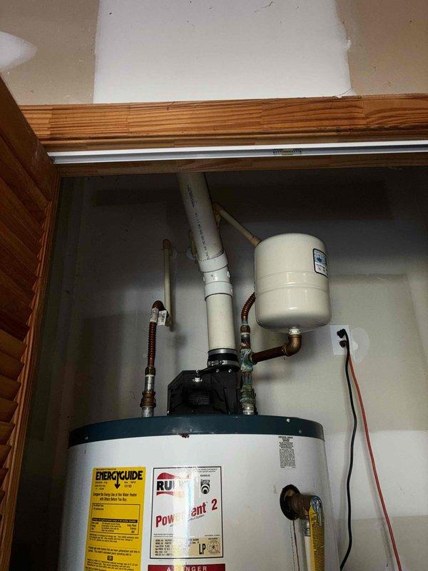 Responded to no hot water complaint at residential property. Upon arrival, inspected tanked water heater installation located in utility cabinet. Verified electrical supply by checking breaker panel - confirmed breaker was functioning properly and in correct position. Performed diagnostic assessment of water heater unit and associated plumbing components including PVC piping, expansion tank, and copper supply lines. Observed significant corrosion on vertical piping with blue-green oxidation, mineral deposits, and rust staining present. Noted deterioration at pipe penetration point with heavy oxidation radiating from base connection. Inspected circulation pump assembly and brass fittings for proper operation. Documented equipment condition through photographic evidence showing corrosion patterns and component wear. Advised customer of findings and recommended monitoring for potential future repairs due to advanced corrosion observed on piping system. Unit operational upon completion of 