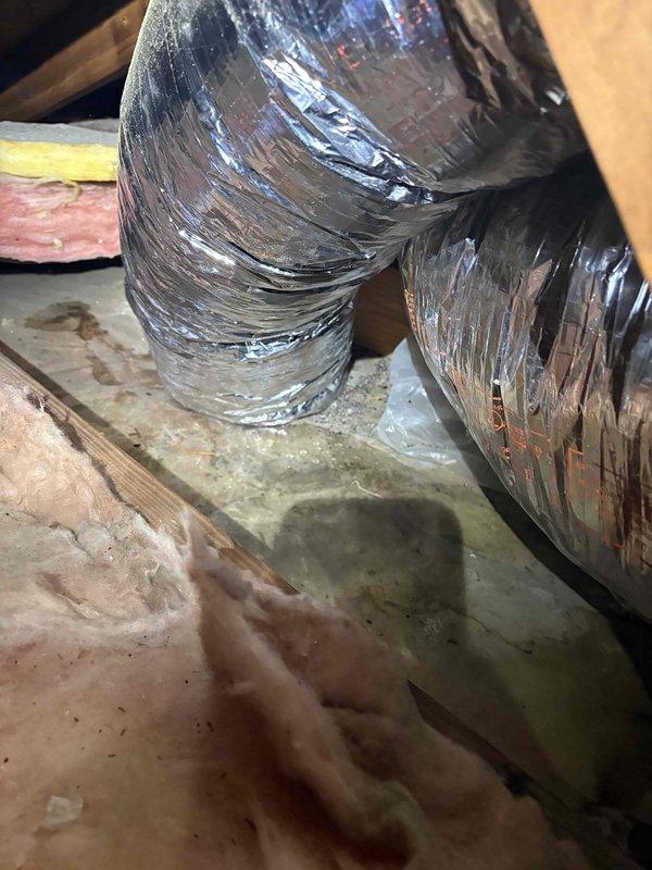 Responded to report of water leak originating from attic space and penetrating through ceiling. Upon inspection, confirmed leak source was HVAC unit rather than roofing system. Examined flexible ductwork installation in attic, noting deteriorated insulation wrap and compromised duct connections. Documented condition of metallic flex duct showing wear patterns and areas where reflective coating had degraded. Observed fiberglass insulation displacement around ductwork with visible moisture exposure and debris accumulation on surrounding surfaces. Inspected duct collar connections and identified potential condensation issues contributing to water intrusion through ceiling below.