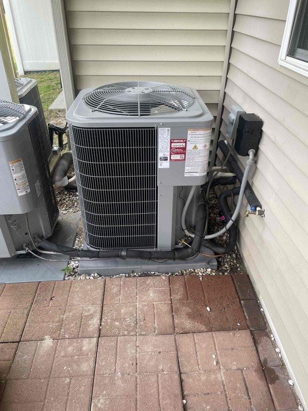 Completed installation of Carrier 2.5-ton 15 SEER air conditioning system with evaporator coil at residential property. Removed and disposed of existing outdoor unit, installed new Carrier 26SCA530WOO3 condenser on pressure-treated wood platform with paver stone base, and installed Carrier CAAMP3017 evaporator coil above existing furnace in interior mechanical closet.

Fabricated and installed metal duct transitions to adapt new coil to existing ductwork system. Replaced outdoor electrical disconnect box and whip to meet current code requirements. Reused existing refrigerant line set, condensate drain lines, and power supply connections after inspection and verification of proper function. Connected and tested all electrical connections between indoor and outdoor components.

Installed black condensate drain pan beneath evaporator coil with proper PVC drainage plumbing. Secured refrigerant lines along exterior wall with appropriate insulation and protection. Verified proper clearances 