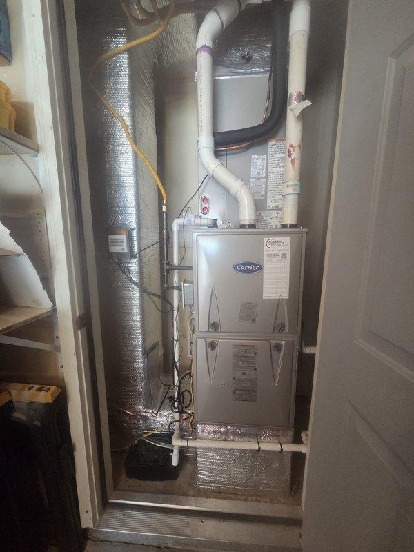 Completed installation of Carrier 2.5-ton 15 SEER air conditioning system with evaporator coil at residential property. Removed and disposed of existing outdoor unit, installed new Carrier 26SCA530WOO3 condenser on pressure-treated wood platform with paver stone base, and installed Carrier CAAMP3017 evaporator coil above existing furnace in interior mechanical closet.

Fabricated and installed metal duct transitions to adapt new coil to existing ductwork system. Replaced outdoor electrical disconnect box and whip to meet current code requirements. Reused existing refrigerant line set, condensate drain lines, and power supply connections after inspection and verification of proper function. Connected and tested all electrical connections between indoor and outdoor components.

Installed black condensate drain pan beneath evaporator coil with proper PVC drainage plumbing. Secured refrigerant lines along exterior wall with appropriate insulation and protection. Verified proper clearances 