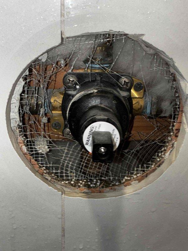 Responded to rental property for two reported issues in master bathroom: no hot water and loose shower handle preventing temperature adjustment. Accessed shower valve through wall opening to diagnose hot water supply issue isolated to master bathroom while rest of house had proper hot water function. Inspected and tightened loose shower handle mechanism to restore proper temperature control operation. Documented existing conditions with photos showing valve assembly access point and plumbing components for reference.