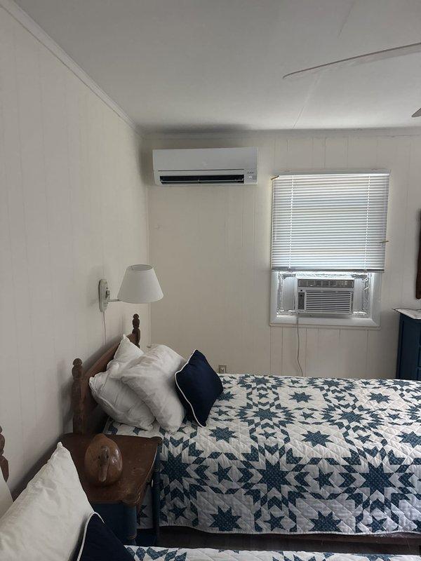 Removed and disposed of existing window air conditioning unit from bedroom. Relocated outdoor heat pump unit to left side of property with back facing ocean, extending existing electrical service to new location and reusing existing equipment stand. Installed new Mitsubishi 9,000 BTU 25 SEER ductless mini-split system consisting of one MUZ-GX09NL outdoor heat pump unit and one MSZ-GX09NL wall-mounted indoor air handler with remote thermostat control. Routed refrigerant lines along exterior of structure to connect relocated outdoor unit to indoor air handler mounted on bedroom wall. System tested and confirmed operational with one-year warranty coverage on ductless equipment from installation date.