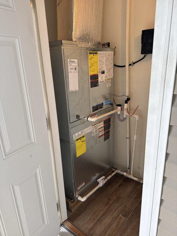 Successfully completed full HVAC system installation featuring a Magic Pak MHP7-7-11-24P 2-ton contained packaged unit in interior utility closet. Installed new air handler unit with vertically stacked configuration, including replacement sleeve for future serviceability. Connected reflective silver-insulated ductwork to upper portion of system for proper air distribution throughout residence. Installed white PVC condensate drainage piping along wall with proper pitch and termination. Ran black electrical conduit and wiring to power system per code requirements. Mounted and programmed Honeywell Digital S1200 thermostat for optimal climate control. Secured all manufacturer labels and safety warnings on equipment panels. Verified all connections, tested system operation, and confirmed proper airflow and drainage function. Installation completed in confined space with professional wire management and clean routing of all utilities. System operational and ready for service.