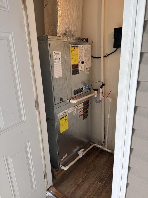 Successfully completed full HVAC system installation featuring a Magic Pak MHP7-7-11-24P 2-ton contained packaged unit in interior utility closet. Installed new air handler unit with vertically stacked configuration, including replacement sleeve for future serviceability. Connected reflective silver-insulated ductwork to upper portion of system for proper air distribution throughout residence. Installed white PVC condensate drainage piping along wall with proper pitch and termination. Ran black electrical conduit and wiring to power system per code requirements. Mounted and programmed Honeywell Digital S1200 thermostat for optimal climate control. Secured all manufacturer labels and safety warnings on equipment panels. Verified all connections, tested system operation, and confirmed proper airflow and drainage function. Installation completed in confined space with professional wire management and clean routing of all utilities. System operational and ready for service.
