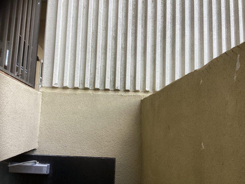 Conducted on-site evaluation for mini split installation at multi-story residential building with textured stucco exterior and corrugated metal siding. Assessed exterior wall conditions, structural mounting requirements, and optimal placement for outdoor condenser unit near building corner with consideration for existing ventilation openings and architectural features.