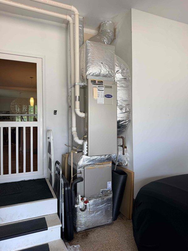 Completed full HVAC system replacement for 15-year-old unit with leaking coil. Installed new Carrier heating unit and air handler in garage/utility area with proper PVC condensate drainage and foil-wrapped ductwork connections. Installed new outdoor condenser unit on gravel pad with wooden frame containment, connected to exterior electrical service, and verified all refrigerant lines and system operations.