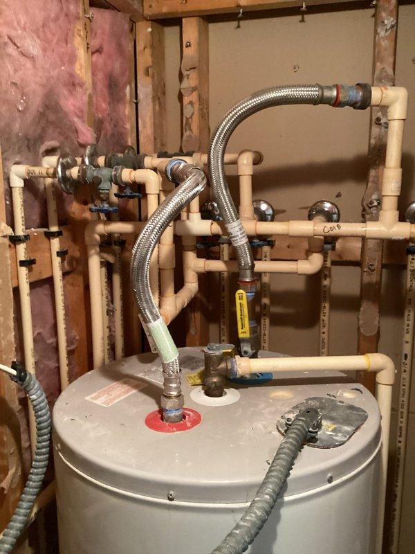 Completed estimate for water heater replacement in residential utility space. Assessed existing tank-style water heater with overhead CPVC manifold distribution system featuring multiple branch lines and shut-off valves. Estimate includes replacement of water heater unit, installation of new supply line shut-off valves, and replacement of flex connectors. Documented current installation configuration showing complex pipe network with blue-handled isolation valves throughout system. Photographed existing conditions for replacement specifications and material requirements.