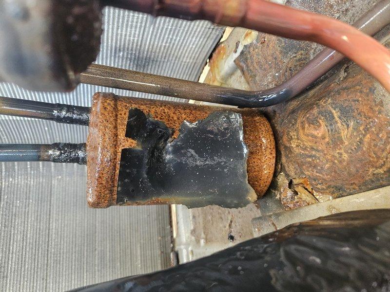 Responded to no cooling complaint on multi-zone system where apartment zone was not functioning while other zone operated normally. Upon inspection, discovered severely corroded evaporator coil and refrigerant line connections with extensive rust damage throughout the affected zone's air handler components. The heavy corrosion on copper refrigerant lines, coil assembly, and connecting hardware indicated prolonged moisture exposure and compromised system integrity. Documented the deteriorated condition of all affected components including the finned coil assembly showing significant oxidation and corrosion buildup at connection points. Advised that the extensive rust damage would require coil replacement and potential refrigerant line repairs to restore cooling function to the non-operational zone.