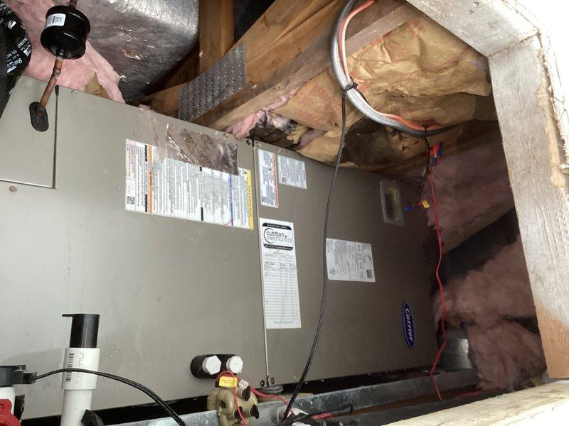 Conducted site assessment for complete HVAC system replacement with air handler relocation from current attic position to bathroom area. Evaluated existing Carrier air handler installation, inspected ductwork that has been spray foamed, and assessed attic conditions including pink fiberglass insulation, copper refrigerant lines, and flexible duct connections. Documented current system configuration and structural considerations for proposed relocation, noting that extensive drywall removal will be required prior to final measurements and equipment sizing. Discussed two replacement options: relocating current forced air system versus installing mini-split units for upper level. Determined that load calculation will be necessary due to building envelope modifications since original installation, including white reflective roofing and spray foam duct insulation, with potential for additional insulation and spray foam application after demolition phase.