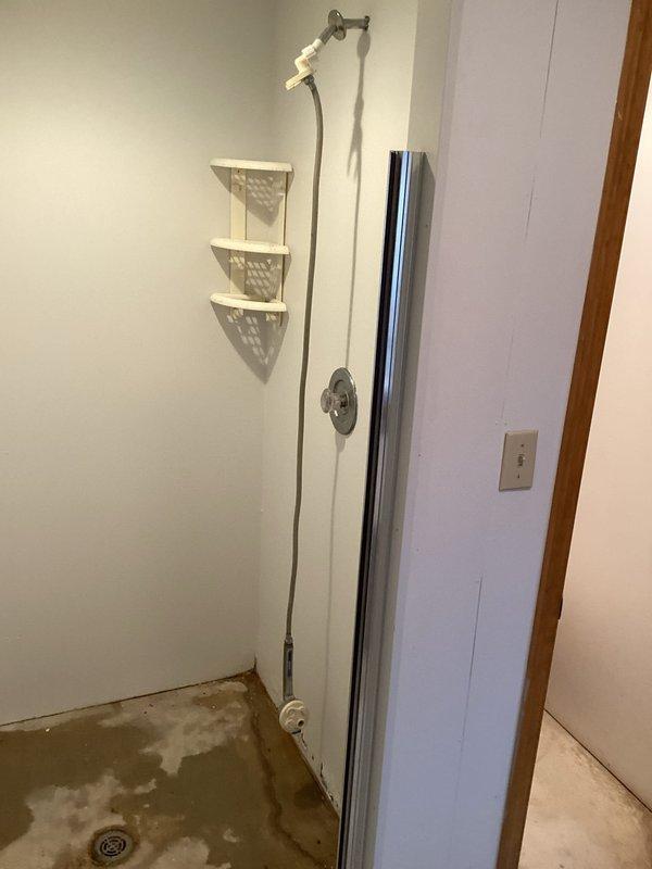 Responded to service call for slow leak in downstairs shower room with water visible along concrete edge between shower and adjacent toilet room. Upon inspection, discovered significant water staining on shower floor indicating ongoing moisture intrusion. Created wall access opening to expose plumbing lines and investigate source of leak behind shower wall. Inspected copper supply lines and drain connections within wall cavity to identify leak location potentially related to previous plumbing work performed at property. Documented conditions with photographs showing extent of shower floor discoloration and exposed plumbing components for further evaluation and repair recommendations.