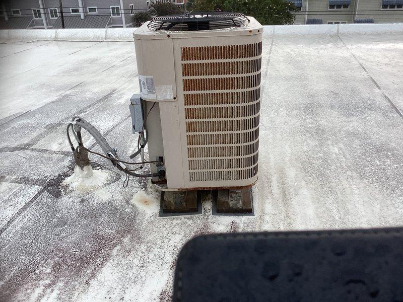Conducted rooftop HVAC system evaluation for commercial building formerly used as furniture store. Assessed existing cylindrical air conditioning condenser unit elevated on wooden blocks, documented condition of electrical connections and wiring, and evaluated rooftop access via metal ladder to roof hatch. Provided comprehensive replacement estimate for complete system installation.