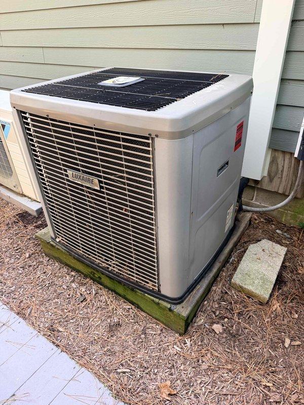 Conducted comprehensive assessment of existing HVAC system for full replacement estimate. Evaluated outdoor Luxaire condensing unit showing age-related wear and weathering on concrete pad with algae growth, along with indoor attic-mounted air handler and associated ductwork. Documented current system configuration including flexible duct routing, electrical connections, and refrigerant lines to provide accurate replacement specifications for main heating and cooling system.