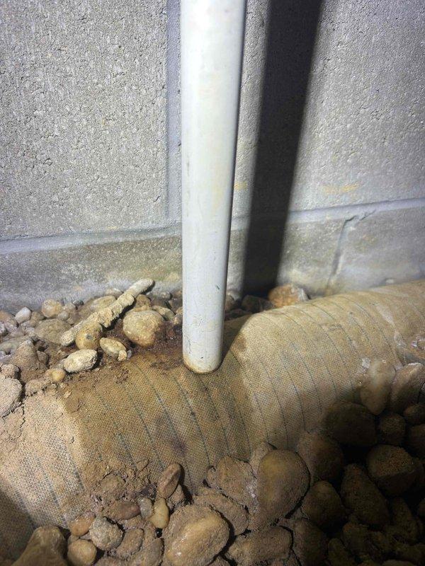 Responded to a no cooling complaint on an HVAC system less than 10 years old. Upon arrival, inspected the condensate drainage system and found the drain line routing through the foundation area. The PVC discharge pipe was properly installed with appropriate fittings and maintained correct pitch for gravity drainage, with the line penetrating through the concrete floor to discharge exterior to the building envelope. Verified the drainage system was functioning as designed with no blockages or standing water present that would trigger a safety float switch and cause system shutdown. All condensate management components were operating within normal parameters.