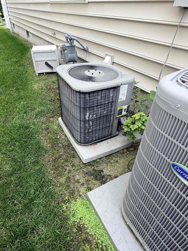 Conducted estimate for replacement of heat pump system located in storage space above garage serving loft area, one bedroom, and one bathroom. Current system is operational but showing age-related wear and deterioration requiring replacement. Accessed unit through wall opening in loft area, assessed existing equipment and installation conditions, documented current outdoor condenser unit configuration with multiple units present on exterior concrete pads, and provided comprehensive replacement options for aging HVAC system.