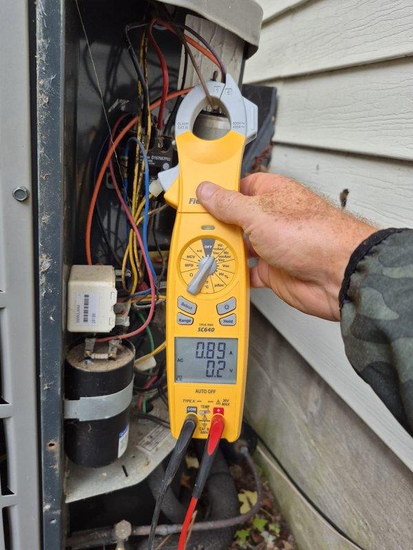 Completed scheduled heating maintenance visit on residential HVAC system. Performed electrical diagnostics using digital multimeter and clamp meter, measuring voltage readings of 15.4V and 23.1V at indoor unit, and current draw of 0.89A at outdoor unit electrical panel. Inspected capacitor, wiring connections, and control components; all measurements within normal operating parameters and system functioning properly.