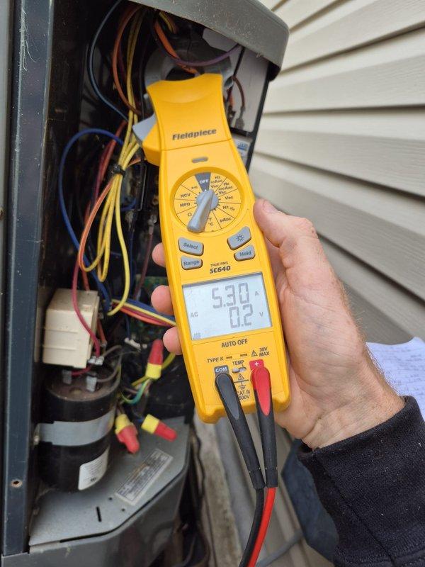Performed seasonal heating maintenance on an 11-year-old heat pump system, inspecting the outdoor condensing unit's electrical compartment, contactor, capacitor, and wiring connections. Measured amperage draw with a clamp meter at both the air handler (21.88 A) and the condensing unit (5.30 A) to verify electrical components were operating within normal parameters. System confirmed operational and ready for heating season.