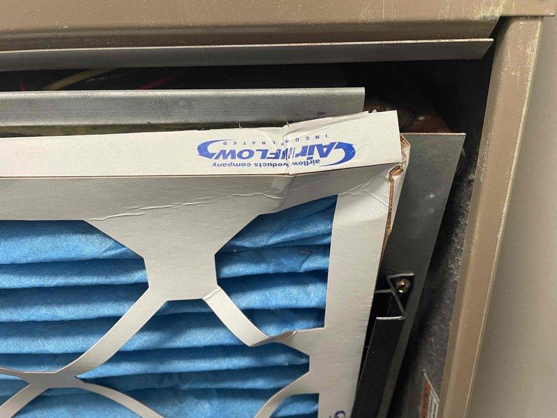 Performed scheduled heating system maintenance on a Magic-Pak packaged HVAC unit, including inspection of the return air filter and filter slot. Found the installed pleated filter with a damaged, creased cardboard frame, sitting askew and bowed in the slot with visible gaps along the edges, which allows unfiltered air bypass. Unit showed light dust and minor scuffing with no rust, ice, or frost, and the condensate drain line was intact. Recommend replacing with a properly sized, undamaged filter to ensure a proper seal and airflow.