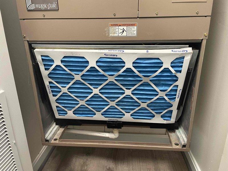 Performed scheduled heating system maintenance on a Magic-Pak packaged HVAC unit, including inspection of the return air filter and filter slot. Found the installed pleated filter with a damaged, creased cardboard frame, sitting askew and bowed in the slot with visible gaps along the edges, which allows unfiltered air bypass. Unit showed light dust and minor scuffing with no rust, ice, or frost, and the condensate drain line was intact. Recommend replacing with a properly sized, undamaged filter to ensure a proper seal and airflow.