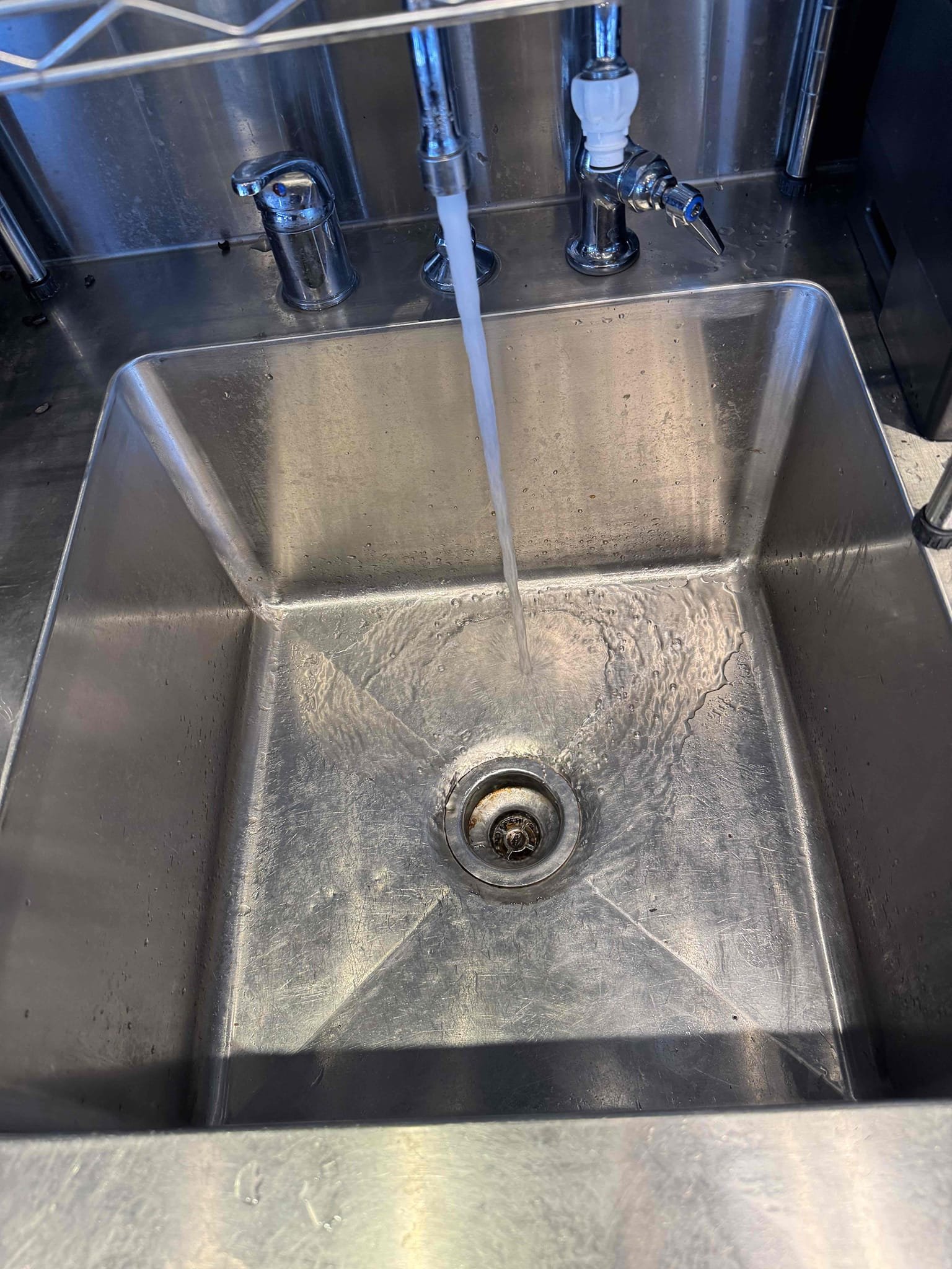 Upon arrival, I identified a clog in the tea urn sink. I used a barrel auger to clear the clog, starting by running it down the strainer and then up to the termination point. After clearing the blockage, I tested the sink to ensure proper drainage. During the inspection, I discovered coffee beans lodged in the sink and the floor sink strainer. I meticulously removed the coffee beans from both areas. Throughout the process, Manager Cassie was present to oversee the work and provide guidance.