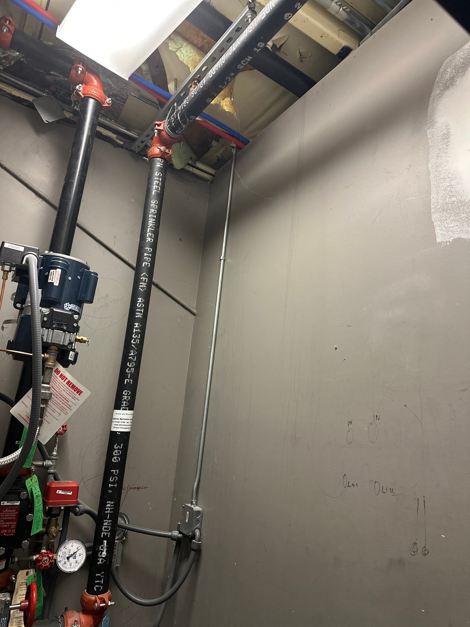 Upon arrival, we identified a 1¼ inch copper water line ascending the right wall in the riser room. To locate the line, we had to navigate through the women’s bathroom. The riser room is situated within the women’s bathroom. We determined that a new Pressure Reducing Valve (PRV) could be installed in the ceiling of the women’s bathroom, on the same wall as the riser room. If necessary, we may need to cut the sheetrock above the drop ceiling to accommodate the PRV and ball valve. Required parts include a 1¼ inch PRV, two 1¼ inch male iron pipe (MIP) copper pipes, a 1¼ inch 90-degree copper pipe, a 1¼ inch copper coupler, thread tape, and pipe dope.