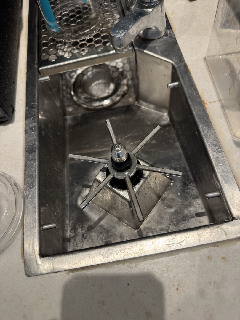 During the service, I identified an issue with the nitro brew drip tray drain line, where plastic tubing was incorrectly used instead of a 90-degree fitting, causing a kink that obstructed water drainage. Additionally, the left rhino rinser was found to be continuously spraying due to a broken bottom flat washer. I removed the rhino rinser, replaced the washer, and reset the system. I also discovered a new drip tray in a box. After removing the old tubing and tray, I installed the new drip tray and repiped using a 1” PVC female adapter, a 90-degree elbow, and 1’ of 1” PVC pipe, connected with a Fernco coupling. I tested the system by pouring water into the tray. Manager Terrence was present during the service.