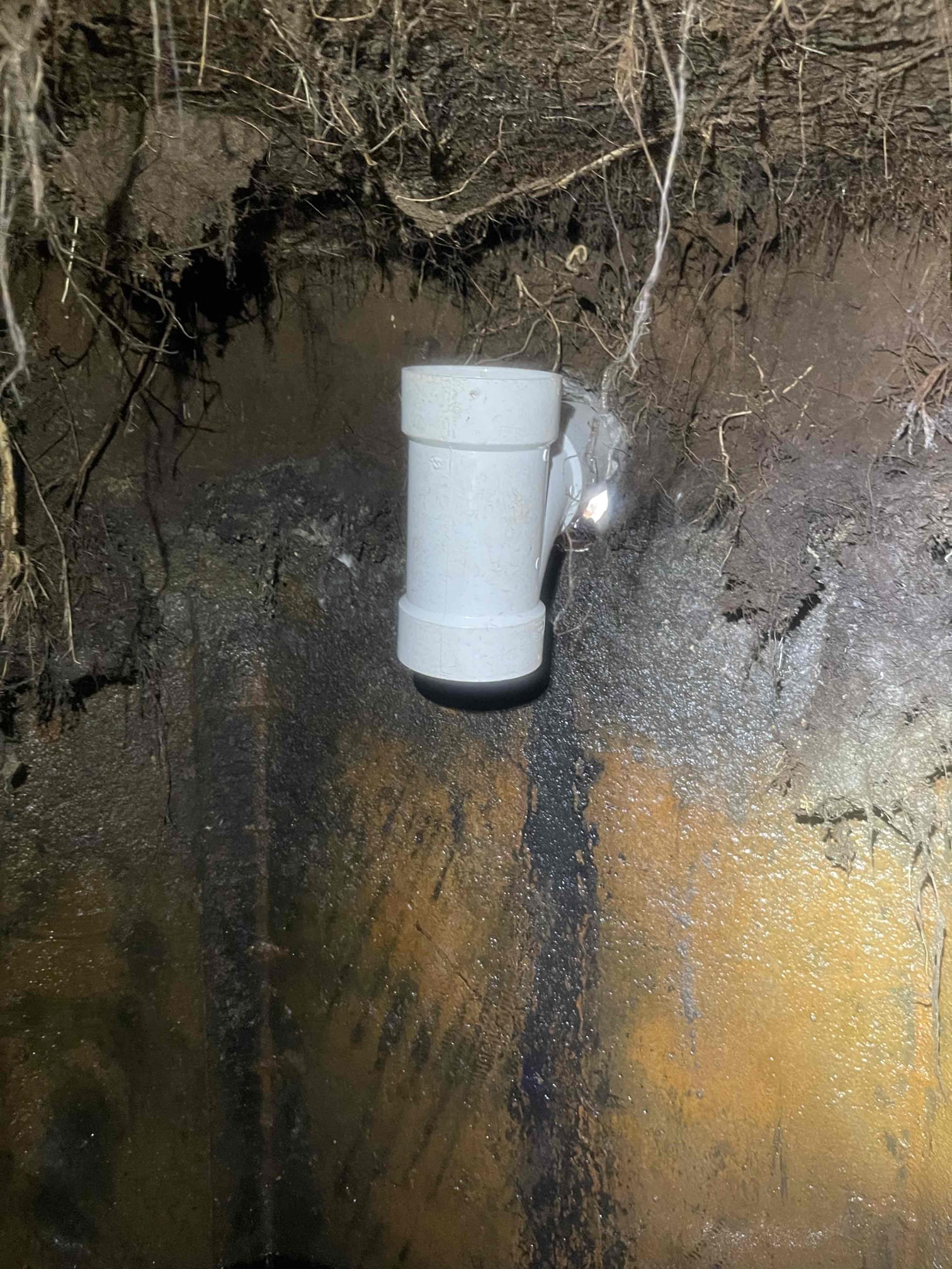 Came out for a sewage back up. Whole house was backing up and sewage was very very slow to drain. Was backing up into the bath tub. Homeowner recently had her septic tank pumped so we knew it was not that. Received approval to pull the toilet and snake/camera the line. Pulled toilet, snaked blockage and got it to drain, ran the camera and found there was a section of cast iron under the concrete patio outside that was heavily rotted and broken as it went into the septic tank. Pipe was full of roots. We received approval to reroute the line. Jack hammered the concrete under the back deck and dug down to the septic tank. Trenched over to the crawlspace and made a new penetration through the wall. Routed 20’ of 4” pvc through the crawlspace, and an additional 8’ down into the septic tank. Climbed into the septic tank and removed the old rotted baffle tee from inside and replaced with pvc. Resealed the penetration with hydraulic cement. Installed two way cleanout outside for future servici