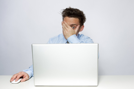 man peeking at a computer screen guiltily