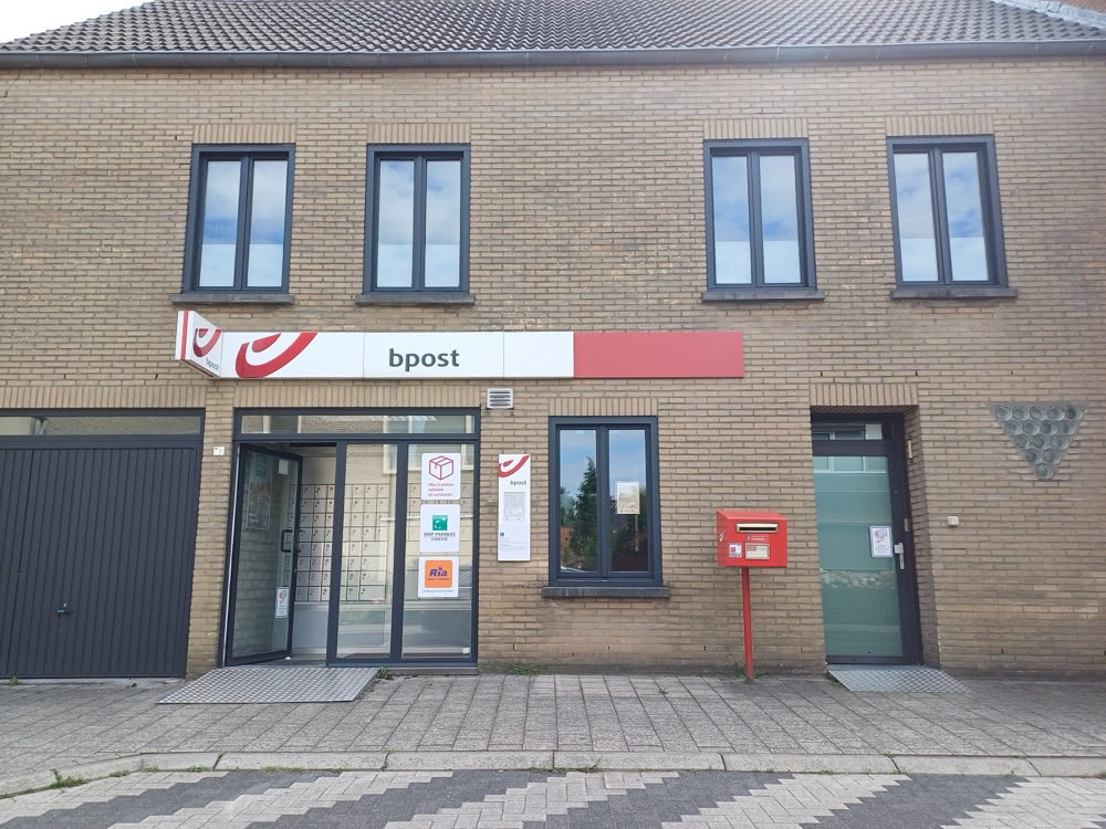 Small bpost post office housed in a brick building in Baarle with a red Belgian mailbox outside.