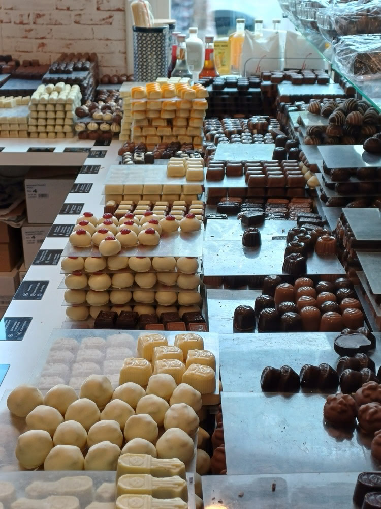 Counter inside a Belgian chocolate shop lined with rows and stacks of assorted pralines