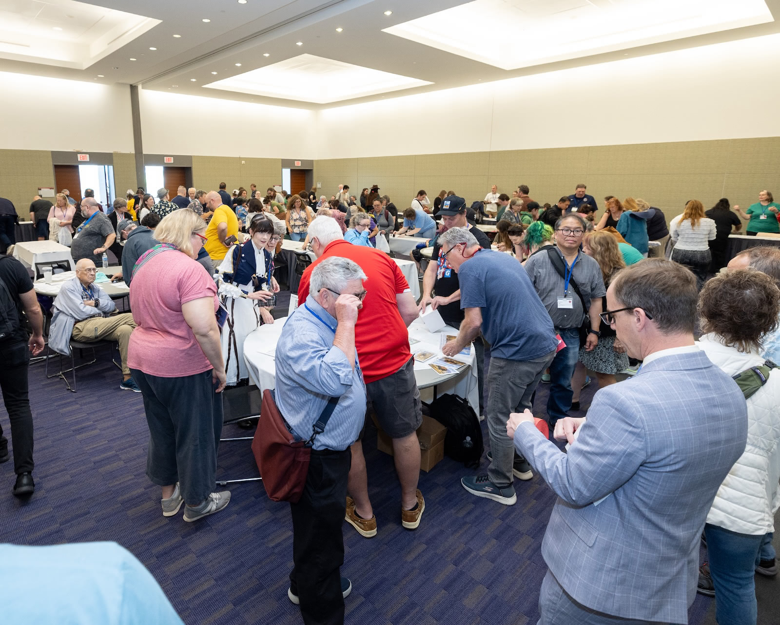A crowded meetup room filled with Postcrossing participants gathering around tables, looking at postcards, stamps, and event materials after the ceremony.