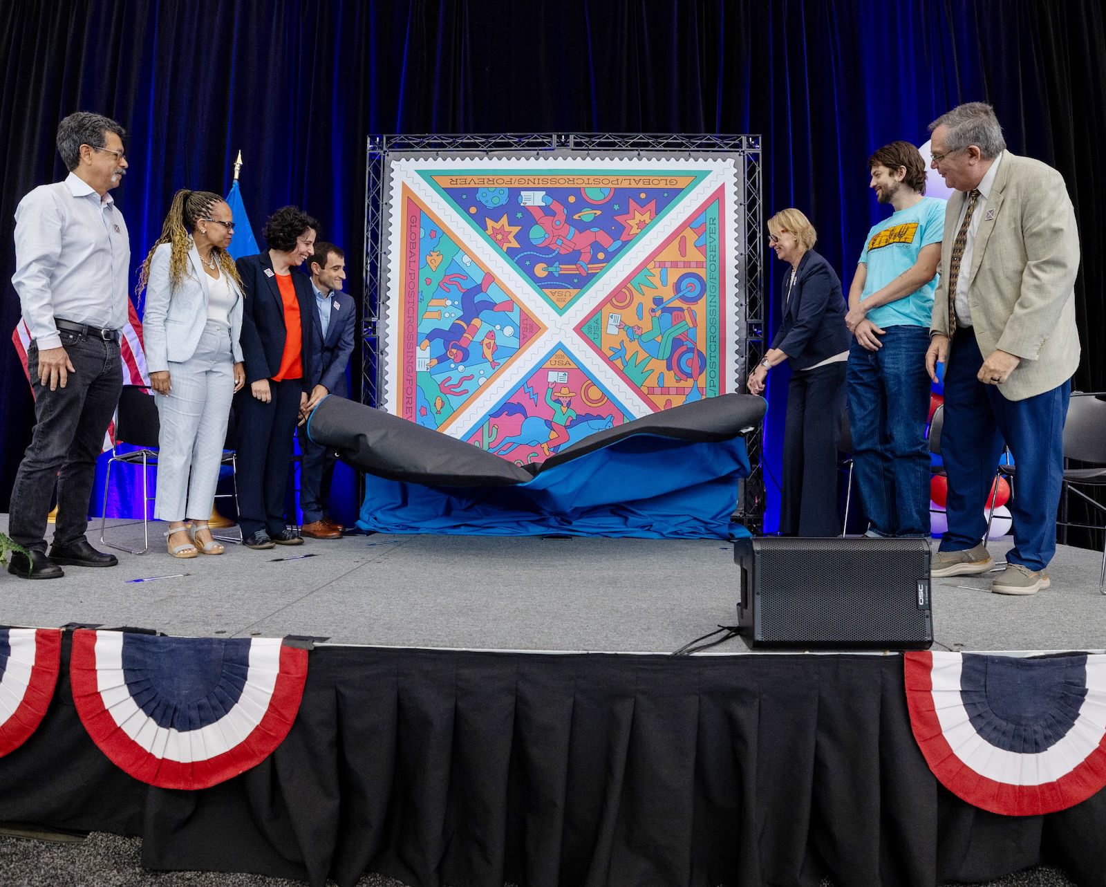 Speakers and guests stand on stage as a large display of the new Postcrossing stamps is unveiled during the dedication ceremony.