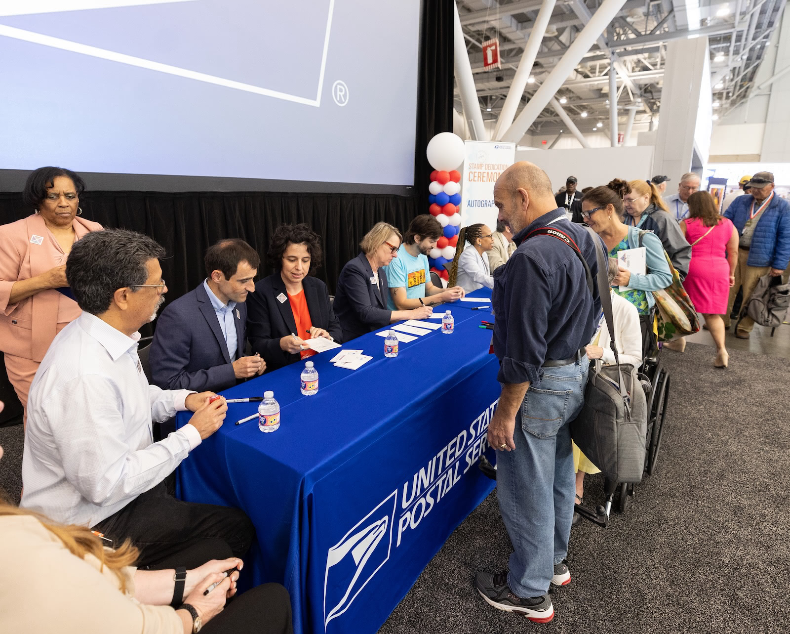 Postcrossing stamp ceremony guests line up at a United States Postal Service table to have event materials signed by speakers and stamp contributors.