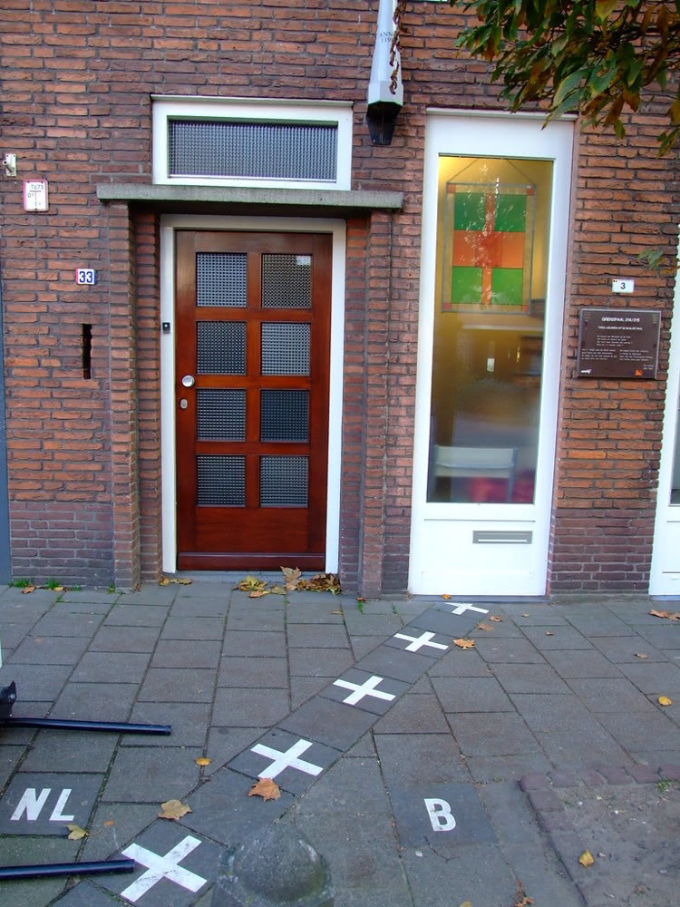 Street border in Baarle marked by white crosses and the letters NL and B running between two neighbouring doorways.