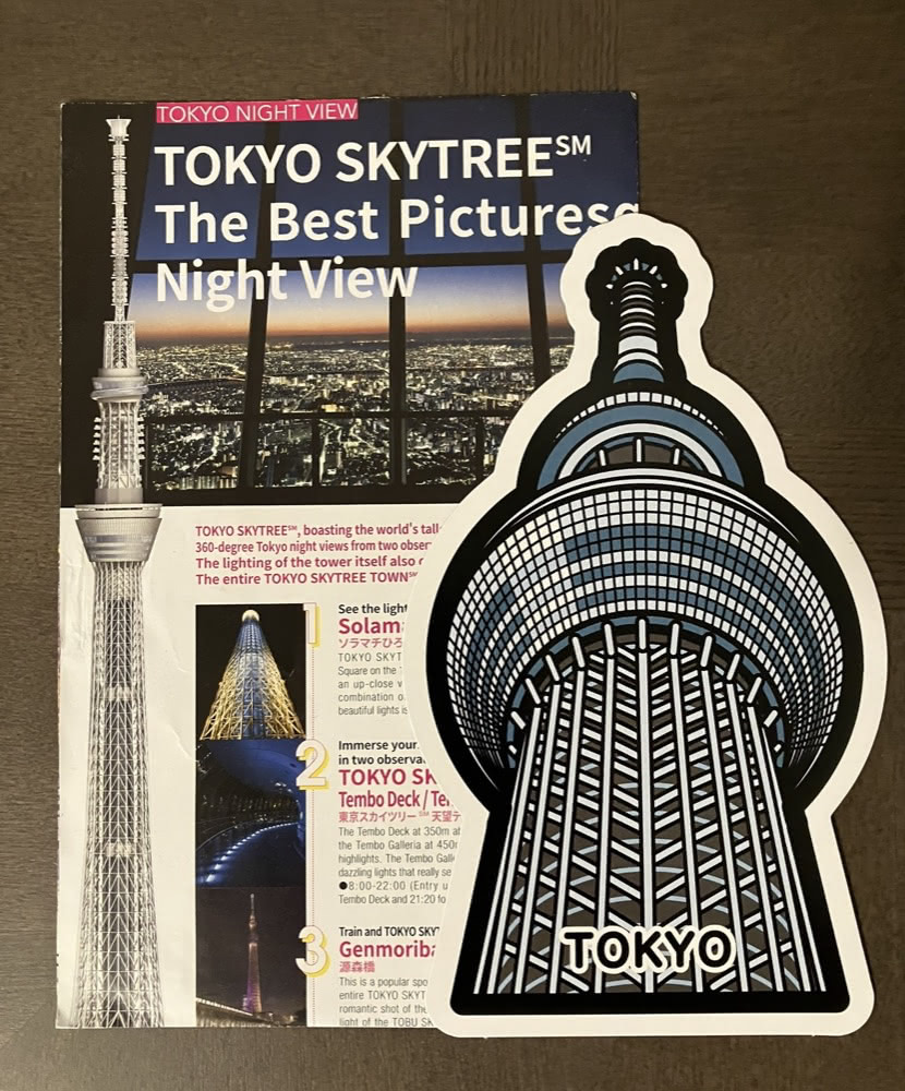 A Tokyo Skytree Gotochi-shaped postcard placed beside a leaflet showing Tokyo Skytree night views.