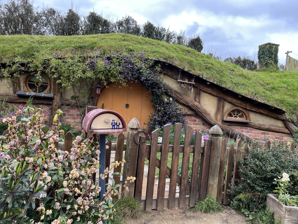 Hobbiton garden gate and hobbit-hole, with a small rounded mailbox in front holding two tiny figures.