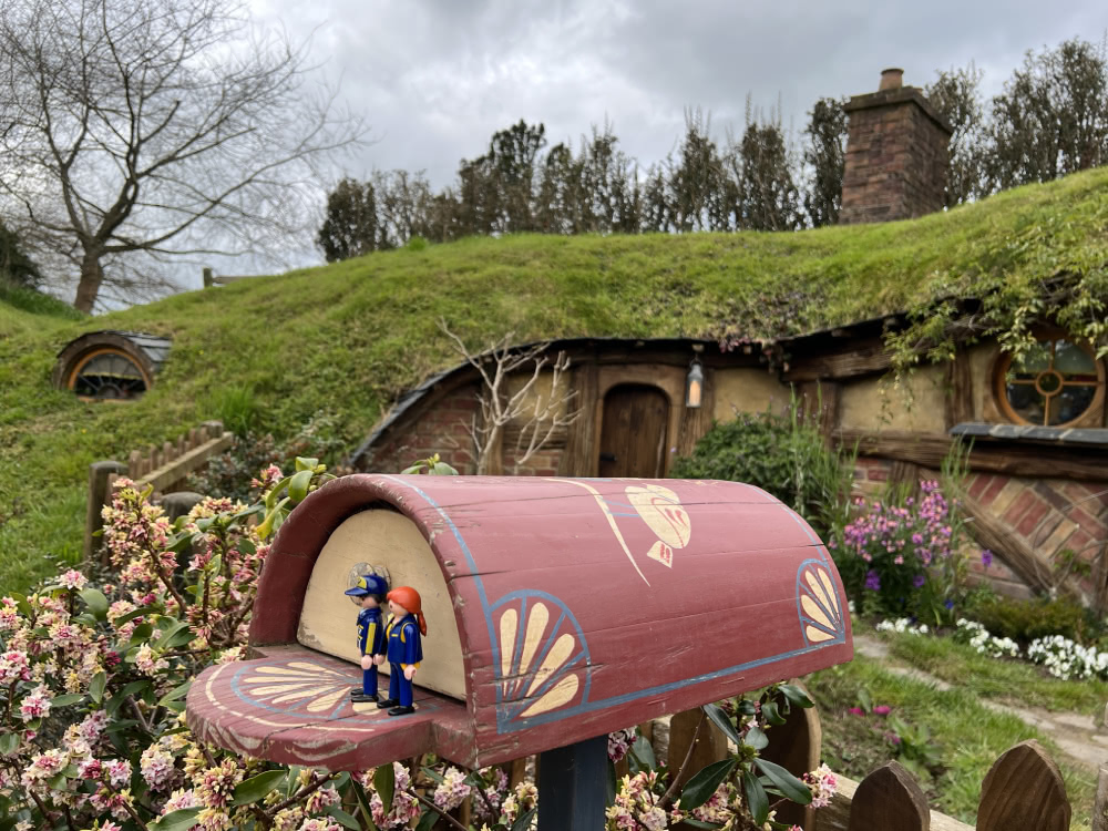 Hobbiton garden gate and hobbit-hole, with the 2 little mail carriers standing in a colorful mailbox