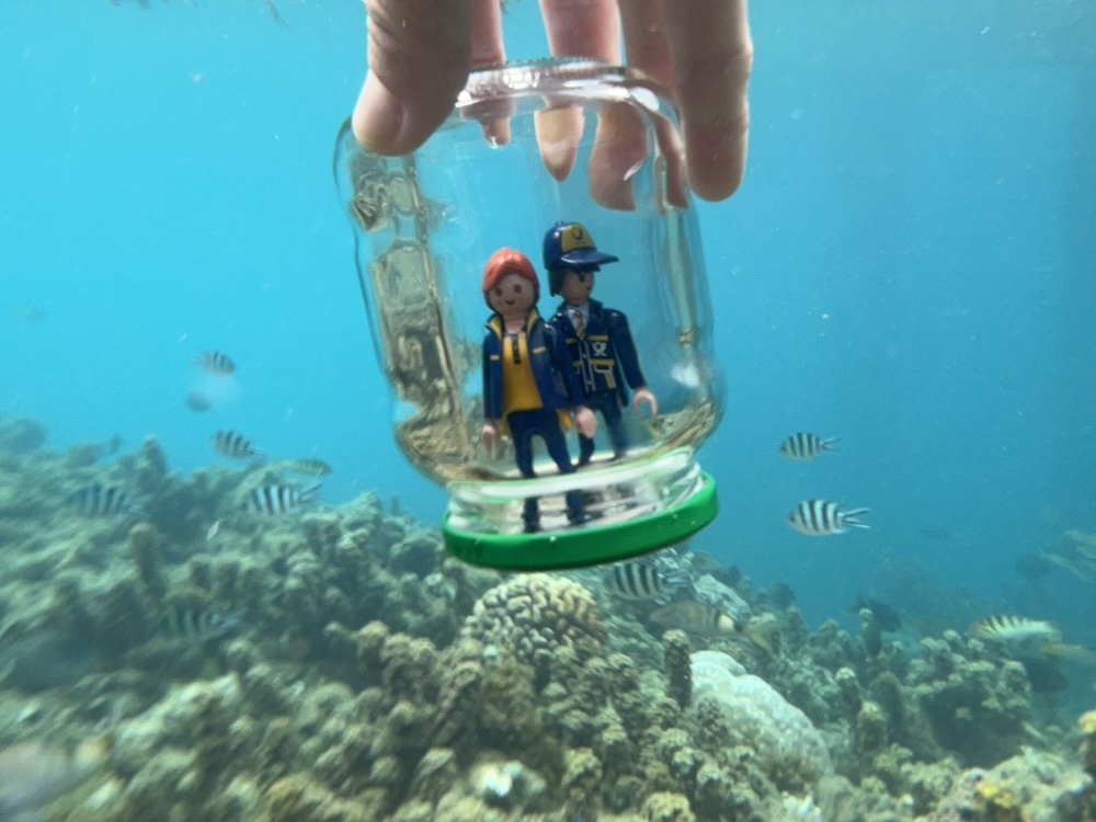 The Little Mail Carrier figures inside a glass jar underwater, surrounded by coral and small striped fish.