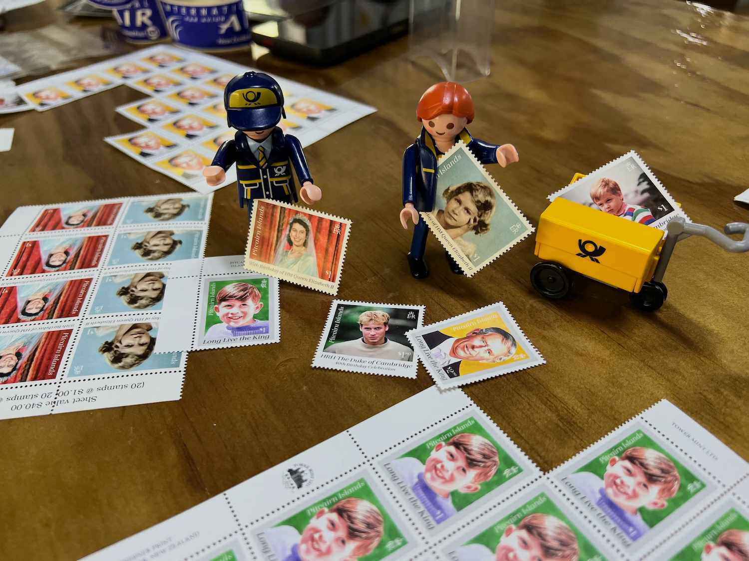 Table covered with postcards, stamp sheets and the Little Mail Carrier figures and their yellow mail cart, ready for postmarking.