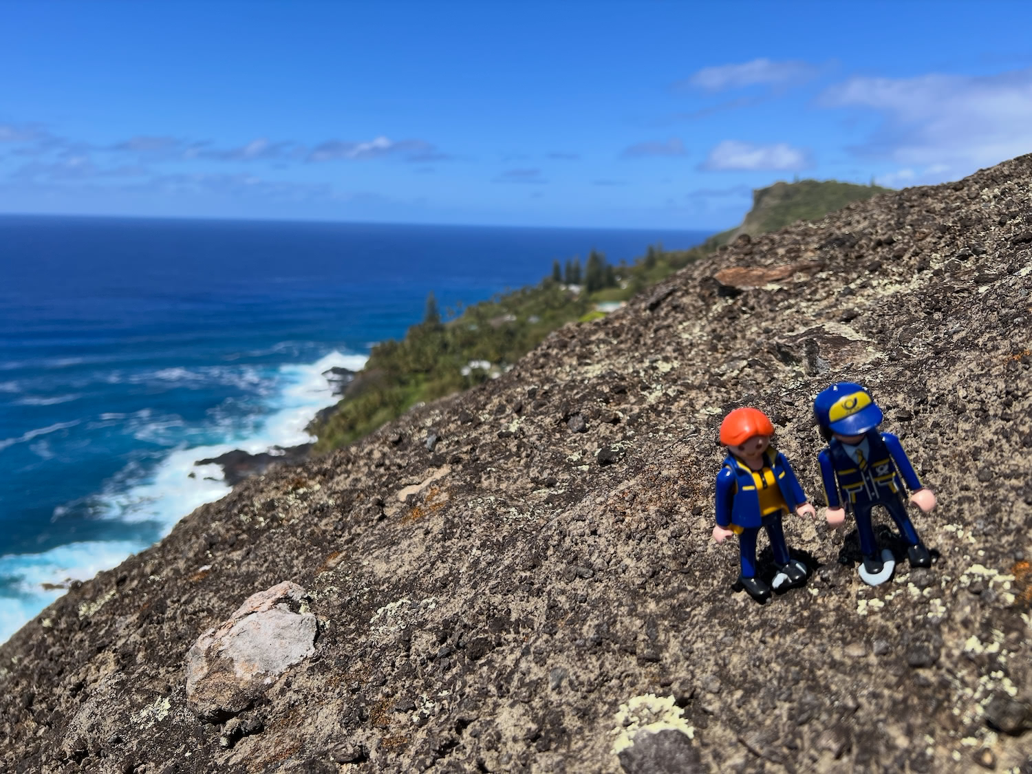 The Little Mail Carriers posing on a rocky hillside overlooking the blue Pacific Ocean around Pitcairn.