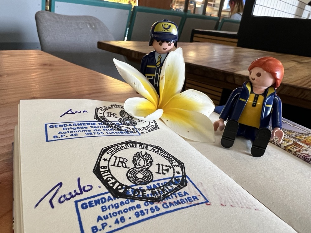 The Little Mail Carrier figures beside a white and yellow flower on a notebook page stamped by the gendarmerie in Mangareva.