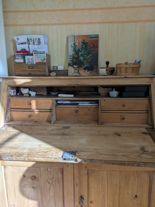 A photo of an old wooden writing desk with many drawers and compartments, full of writing supplies and decorated with a cat painting