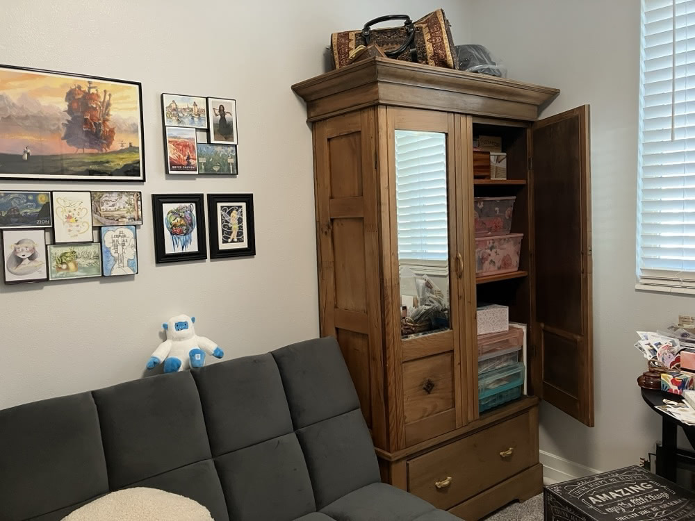 A cozy postcard room with framed art on the wall, a couch and a wooden cabinet used for storing postcard supplies.