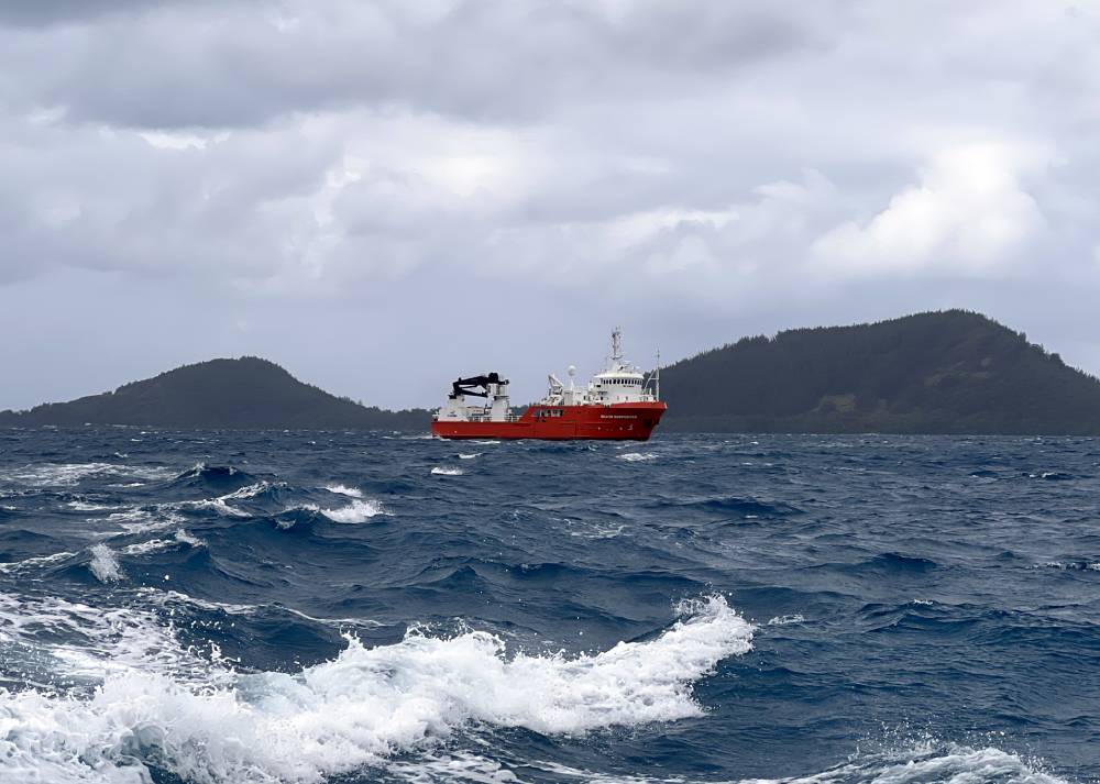 Red-and-white ship on choppy blue water, with green islands in the background under a cloudy sky.