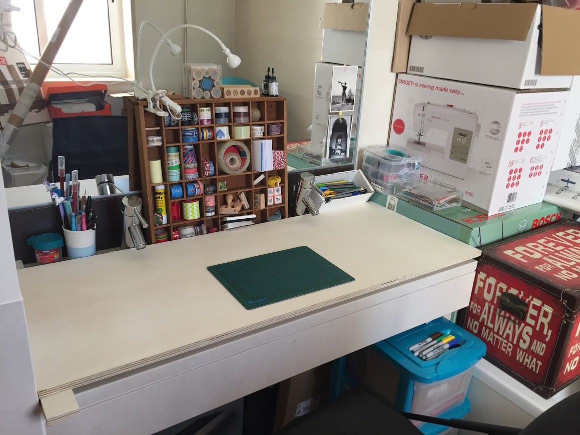 A desk set up by placing a piece of wood over an old sink, so you can still see the taps and the mirror behind; there's a little wooden cabinet full of washi tapes and rubber stamps, and writing/drawing supplies in pots and boxes around