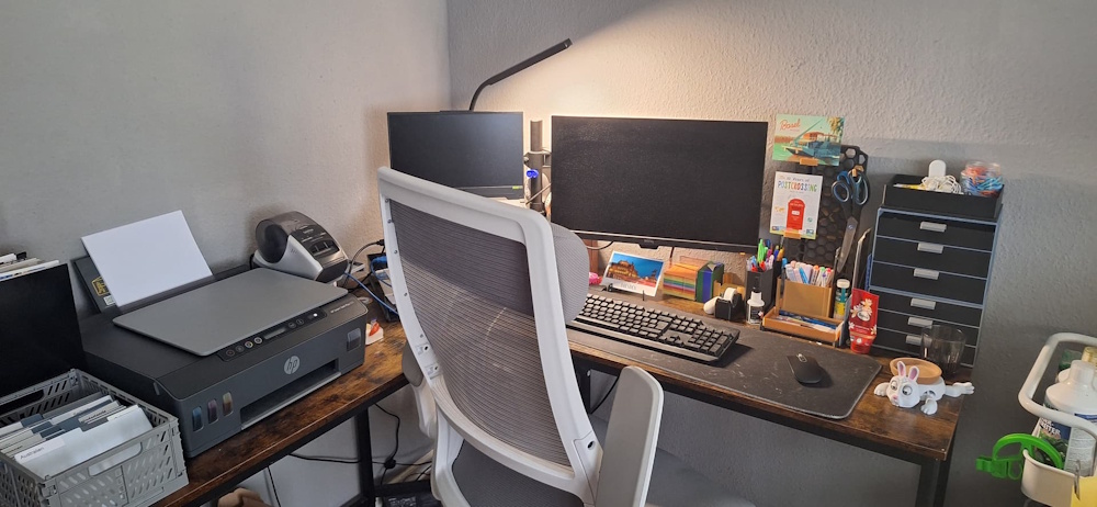 A desk set up in a corner with PC equipment but also supplies for Postcrossing, neatly organised