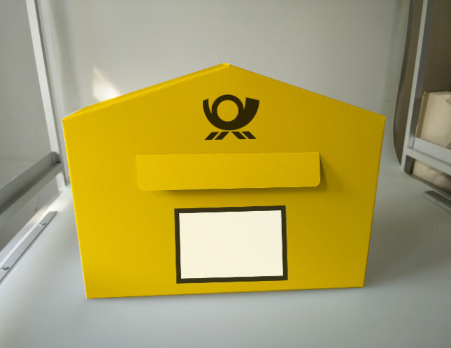 Yellow cardboard Deutsche Post mailbox with post horn logo, mail slot flap, and label window.