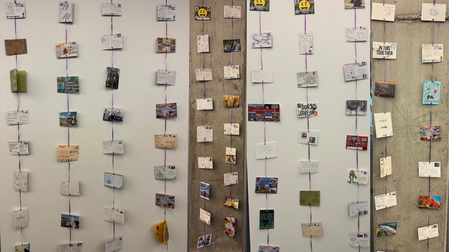 Postcards and handwritten cards hanging in vertical rows on strings along the walls at Geocaching HQ.