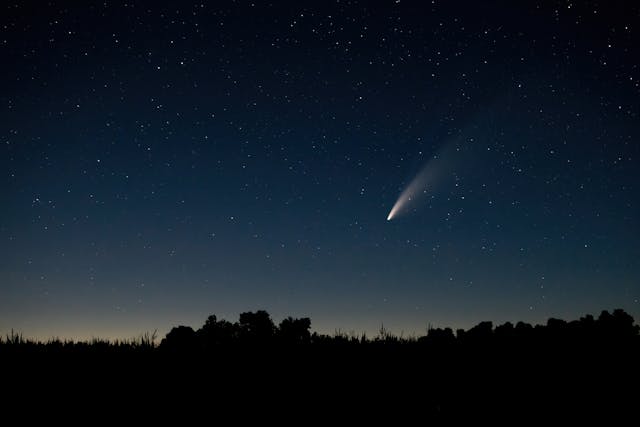 A photograph of the night sky against the horizon, with a comet or meteor streaking downward